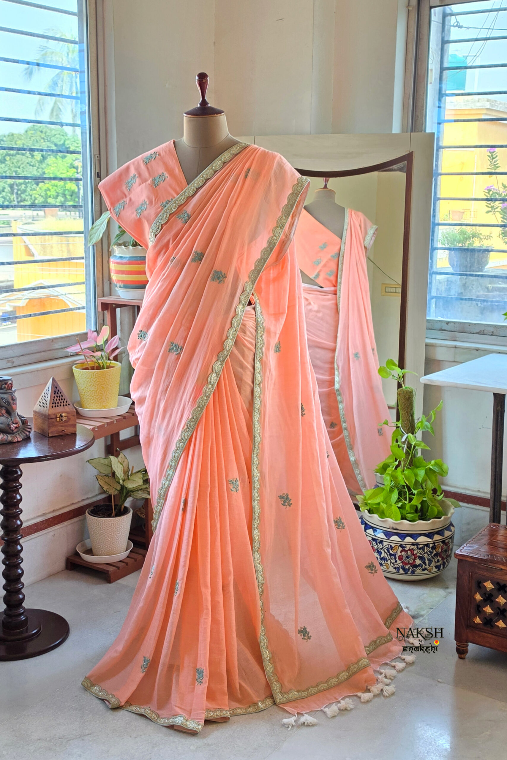 Full length peach blossom pure cotton handloom saree with all over teal embroidery motifs gold scallop border and white tassels displayed on mannequin by Naksh by Enakshi